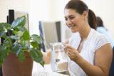 Woman+in+computer+room+watering+plant+smiling