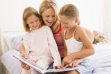 Woman+and+two+young+girls+in+bedroom+reading+book+and+smiling