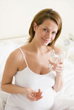 Pregnant+woman+in+bedroom+holding+medicine+and+water+smiling