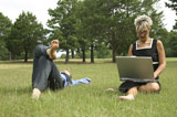 Mid+adult+woman+working+on+a+laptop+with+a+man+lying+in+the+grass+beside+her