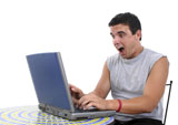 Attractive+young+man+in+casual+sleeveless+t-shirt+sitting+at+bistro+table+working+on+laptop+computer.+Surprised+expression.