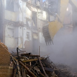 A+backhoe+emerging+from+the+dust+cloud+to+knock+down+the+walls+of+a+historic+apartment+building.+