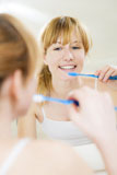 Young+woman+looking+into+a+mirror+brushing+her+teeth