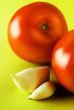 two+tomatoes+with+two+garlic+cloves+on+bright+green+surface