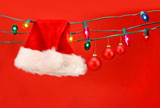 Hanging+lights+with+santa+hat+and+christmas+balls+against+a+red+background