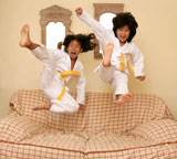 Two+little+asian+judo+dressed+gils+jumping+over+the+sofa+at+home
