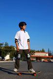 boy+standing+on+a+skateboard+in+an+afternoon+sun+with+blue+sky+in+the+background+