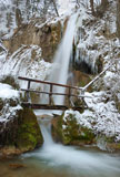 Waterfall+with+icicles+and+snow+around+with+a+small+wooden+bridge+on+a+winter+day.+