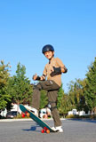 Smiling+teenage+boy+with+his+thumbs+up+standing+on+a+skateboard+on+a+sunny+day+with+blue+sky+and+trees+in+the+background.+
