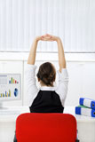 Rear+view+of+young+businesswoman+sitting+at+desk+stretching.+Copy+space+