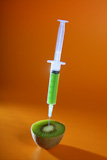 Injection+with+syringe+to+a+green+kiwi+fruit+over+orange+background