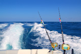 Trolling+fishing+boat+rod+and+golden+saltwater+reels+deep+blue+ocean+sea+wake