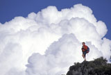 Man+Standing+Atop+Rock+With+Giant+White+Clouds+in+Background