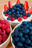 A+bowl+of+healthy+breakfast+strawberries%2C+raspberries+and+blueberries+in+plain+yogurt+with+bowls+of+raspberries+and+blueberries+in+the+foreground