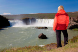 A+young+woman+hiker+by+a+waterfall.+Shot+on+location+at+Godafoss+waterfall+in+Iceland.