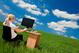 Business+concept+shot+of+a+beautiful+young+woman+sitting+at+a+desk+using+a+computer+in+a+green+field+with+a+bright+blue+sky+with+fluffy+white+clouds.+Shot+on+location.