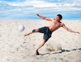 Young+man+playing+soccer+on+beach.