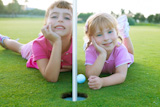 Golf+two+sister+girls+relaxed+lying+near+green+hole+with+ball