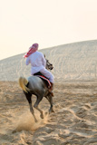 An+anonymous+Arab+man+in+traditional+clothing+riding+his+horse+in+the+sand+of+a+desert+batheed+in+golden+sunlight