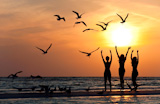 Three+beautiful+young+women+in+bikinis+dancing+on+a+beach+at+sunset+surrounded+by+sea+gull+birds+all+in+silhouette