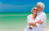 Happy+senior+man+and+woman+couple+together+looking+out+to+sea+on+a+deserted+tropical+beach+with+bright+clear+blue+sky
