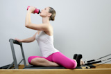 aerobic+gym+pilates+woman+rest+drinking+water+bottle+in+reformer+bed