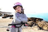 bicycle+little+happy+girl+pink+helmet+in+rocky+beach+sea+Mediterranean