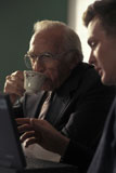 Elderly+Man+Sipping+Tea+While+Young+Man+Uses+Laptop+Computer