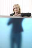 Caucasian+Businesswoman+Standing+Behind+A+Translucent+Blue+Cubicle+And+Smiling+At+You