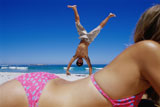 Side+profile+of+a+young+woman+lying+on+the+beach+with+a+young+man+doing+a+handstand+behind+her