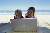 Portrait+of+a+brother+and+sister+lying+in+front+of+a+laptop+on+the+beach