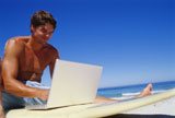 Low+angle+view+of+a+young+man+using+a+laptop+on+a+surfboard