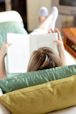Blond woman reading a book lying on a sofa