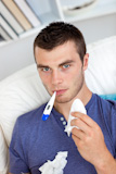 Sick man sitting on the sofa with thermometer and tissues