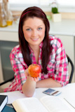Serious woman holding an apple sitting in the kitchen