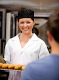 Smiling female baker holding baguettes ready to serve her customer