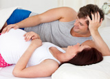 Cute man touching the belly of his pregnant wife lying on the bed at home