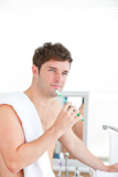 Thoughtful man brushing his tooth with towel on his shoulder