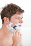 Portrait of a serious man shaving looking away standing in the bathroom