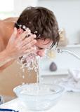 Attractive man spraying water on his face after shaving in the bathroom