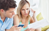Focused couple calculating bills using a calculator sitting on the sofa
