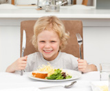 Excited boy holding forks to eat pasta and salad