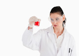 Dark-haired scientist with safety glasses looking at a red beaker