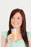 Glad red-haired woman enjoying a glass of orange juice in the kitchen