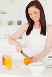Young attractive red-haired woman cutting an orange in the kitchen