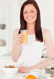 Young attractive red-haired woman drinking a glass of orange juice in the kitchen