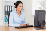 Attractive woman with a headset helping customers while typing on a keyboard