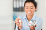 Charming woman holding keys and a miniature house while looking at the camera