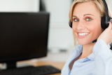 Portrait of a smiling blonde businesswoman with headset working with PC looking into camera
