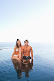 Couple sitting on pool edge with sea in the ط